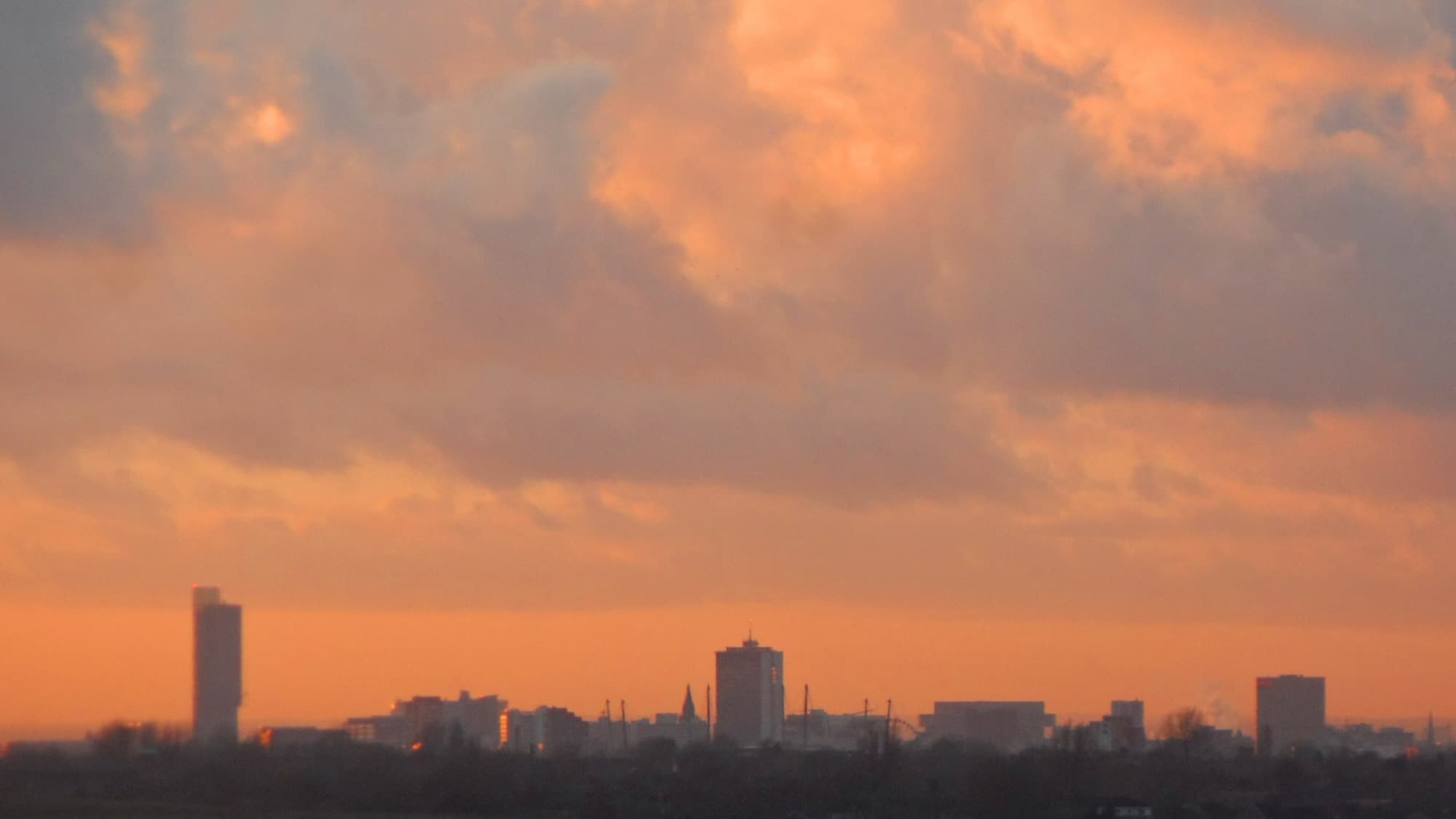 The Manchester and Salford skyline at sunset, towers silhouetted against an orange sky